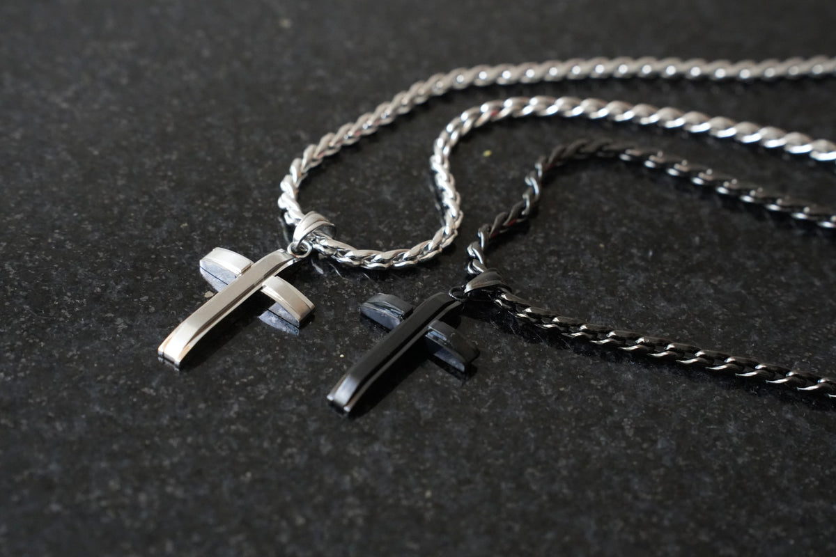 Apex Silver and Black Cross necklaces laid together on dark stone